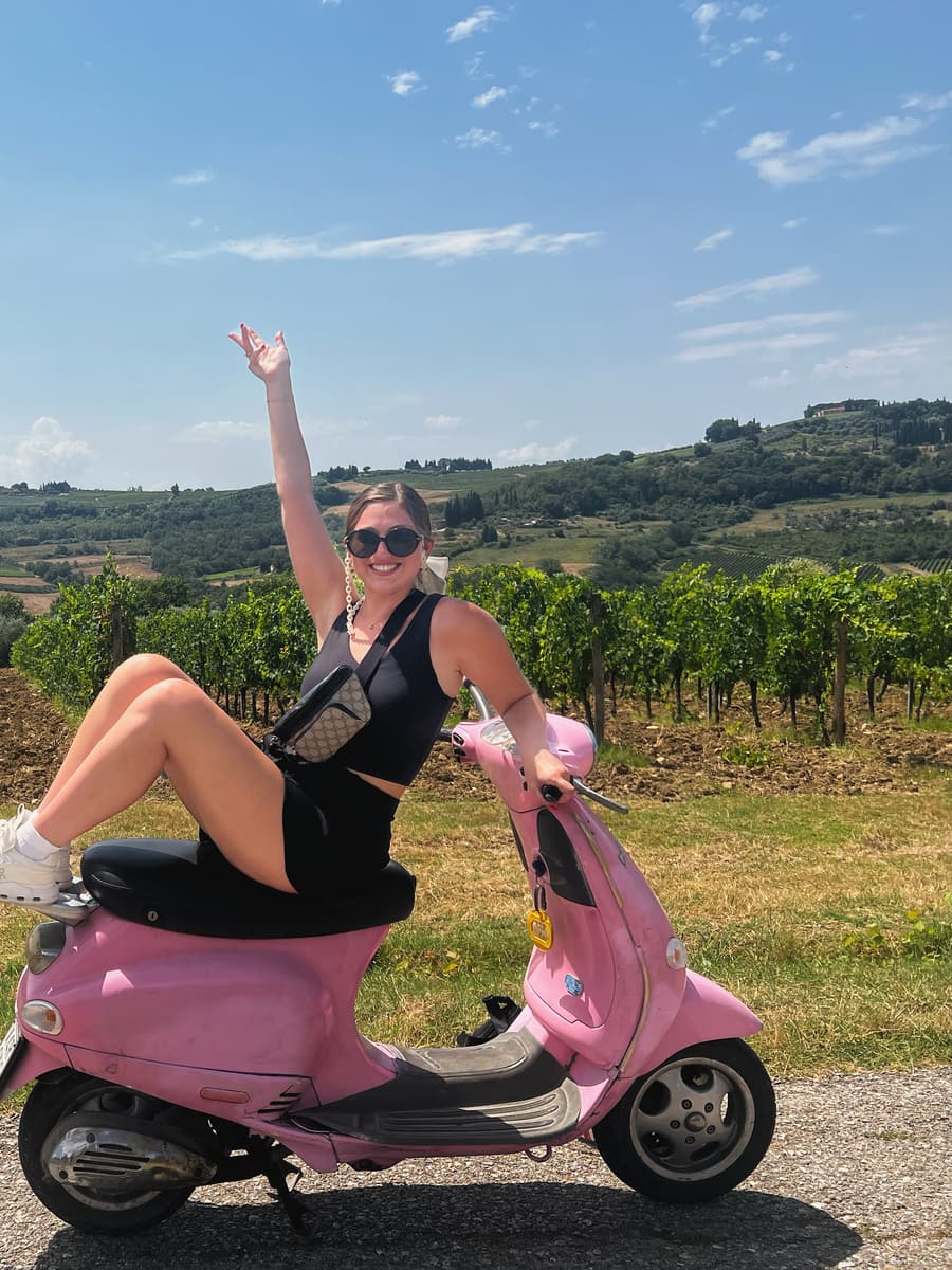 Juliana on a pink Vespa on a road running between vineyard rows