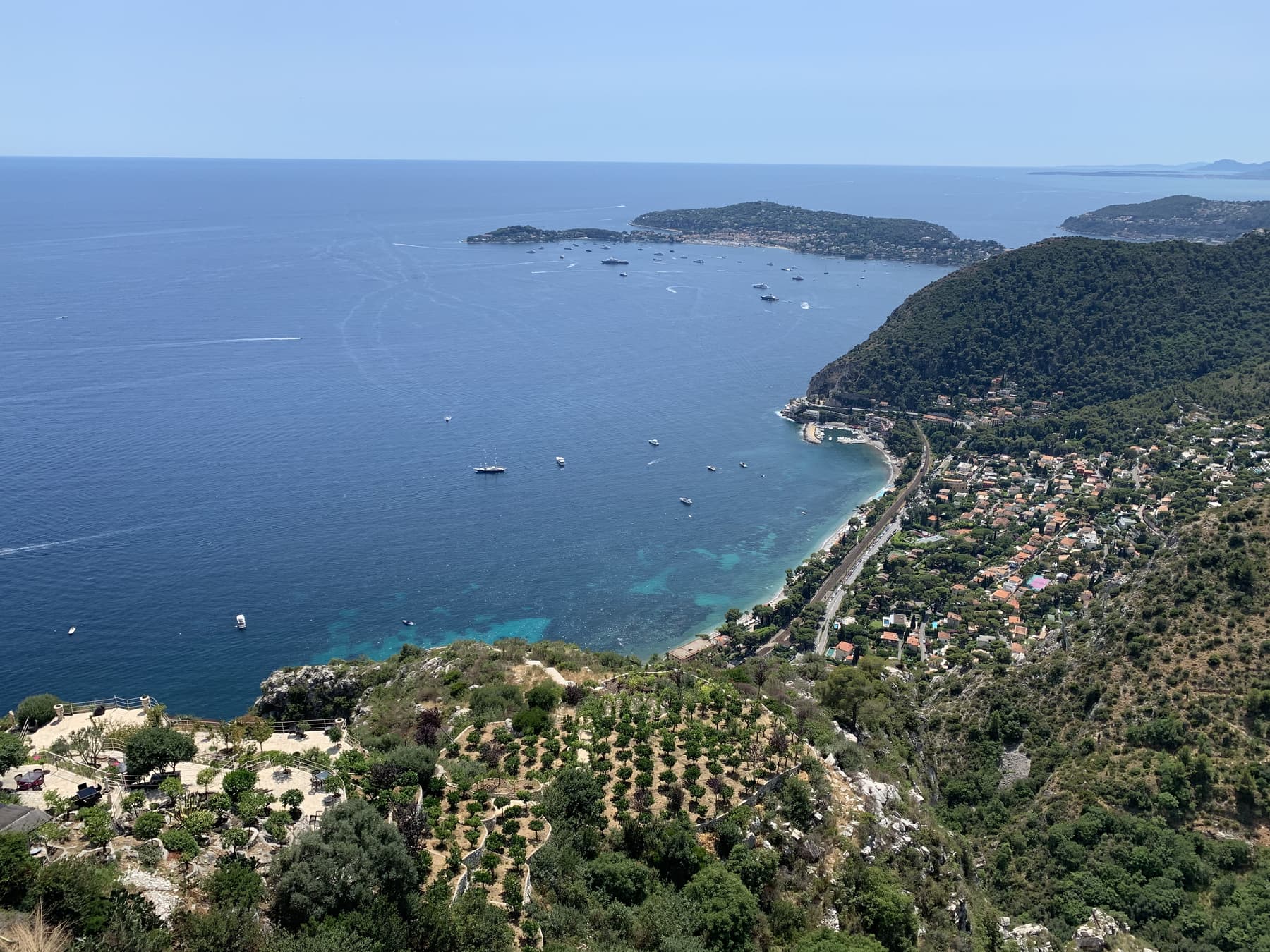 A Mediterranean bay seen from the cliffs above, boats scattered across deep blue water