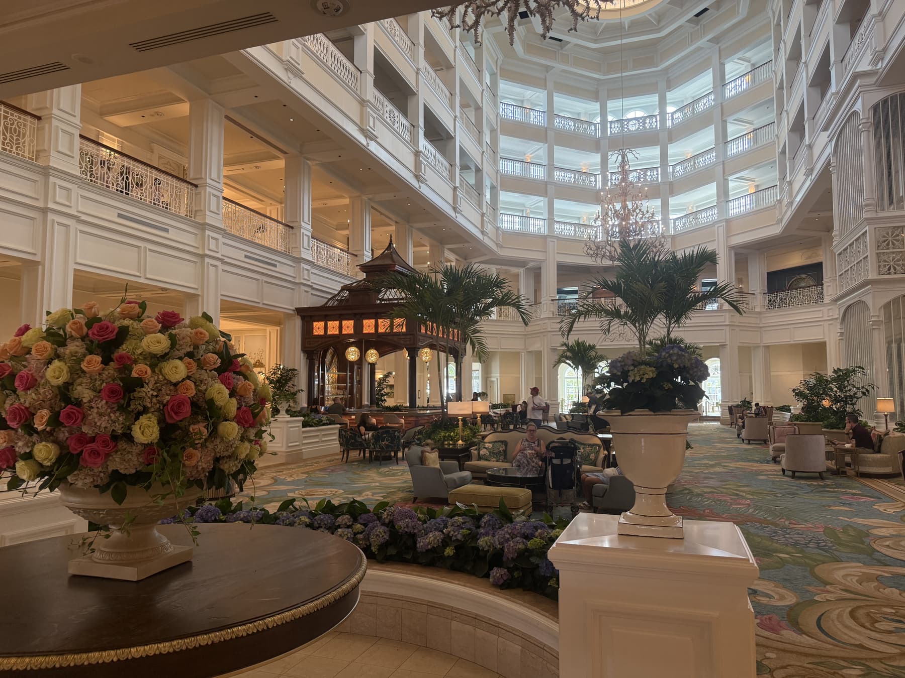 The sunlit lobby of a grand hotel, with a tall floral arrangement at its centre